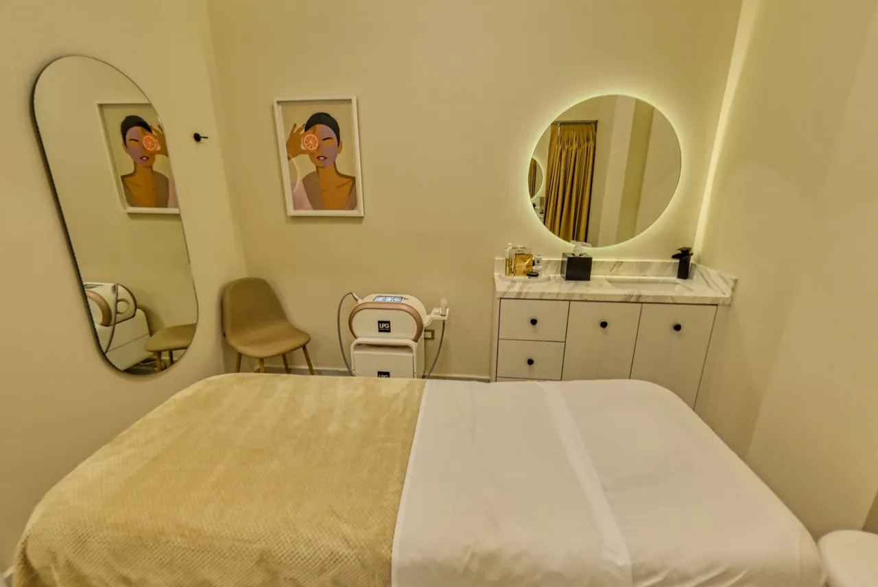 A treatment room with a bed, an LPG device, an oval mirror and a lit round mirror.