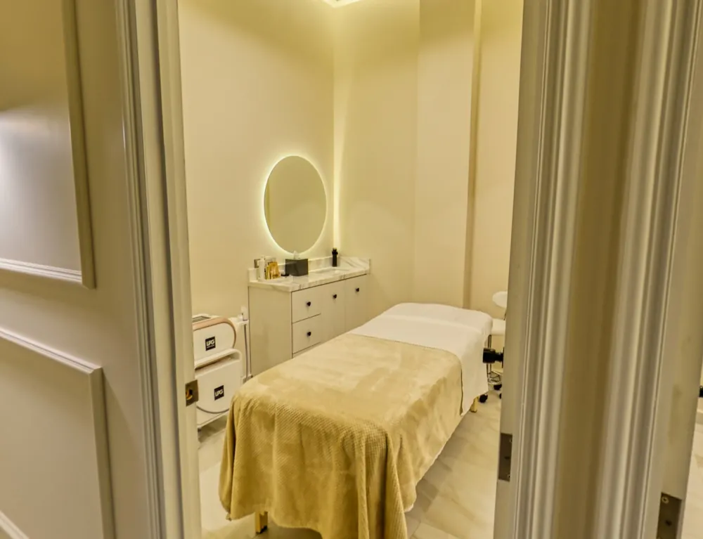 A treatment room seen from its door: the bed, the marble vanity and the lit round mirror.