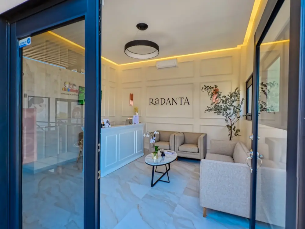 La puerta de cristal abierta desde la pasarela de la plaza, con la recepción y el nombre RaDANTA al fondo.