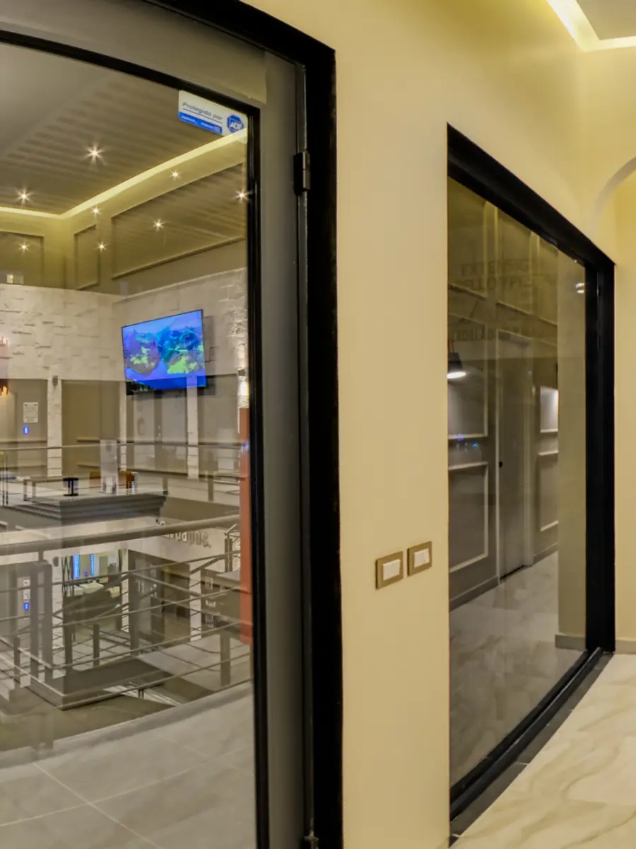 Desde la recepción, la puerta de cristal abierta hacia la pasarela de la planta alta de la plaza.
