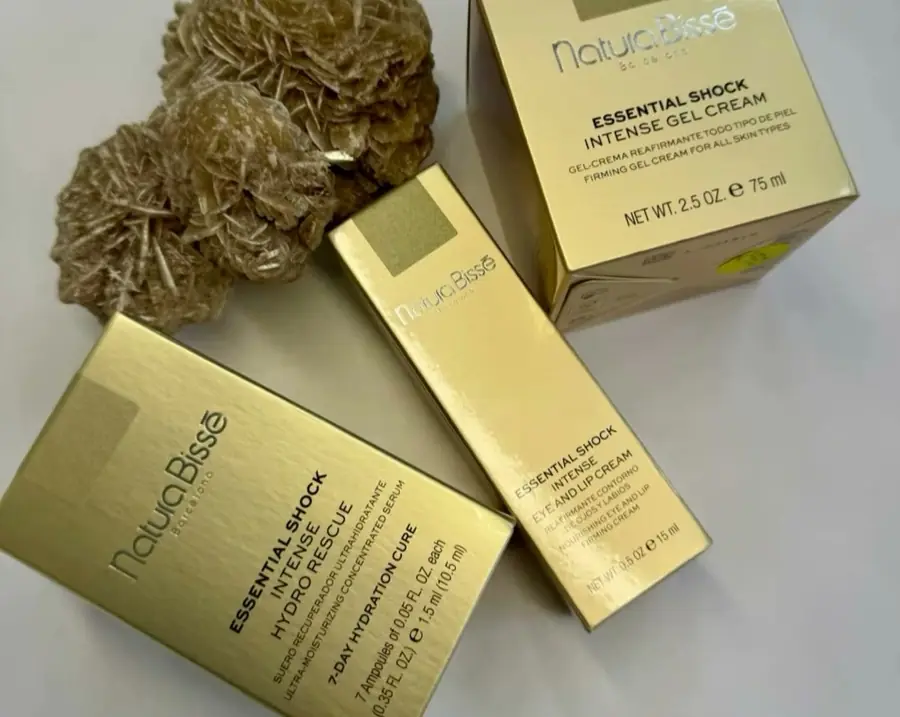Tres cajas doradas de Essential Shock de Natura Bissé junto a unas rosas del desierto.