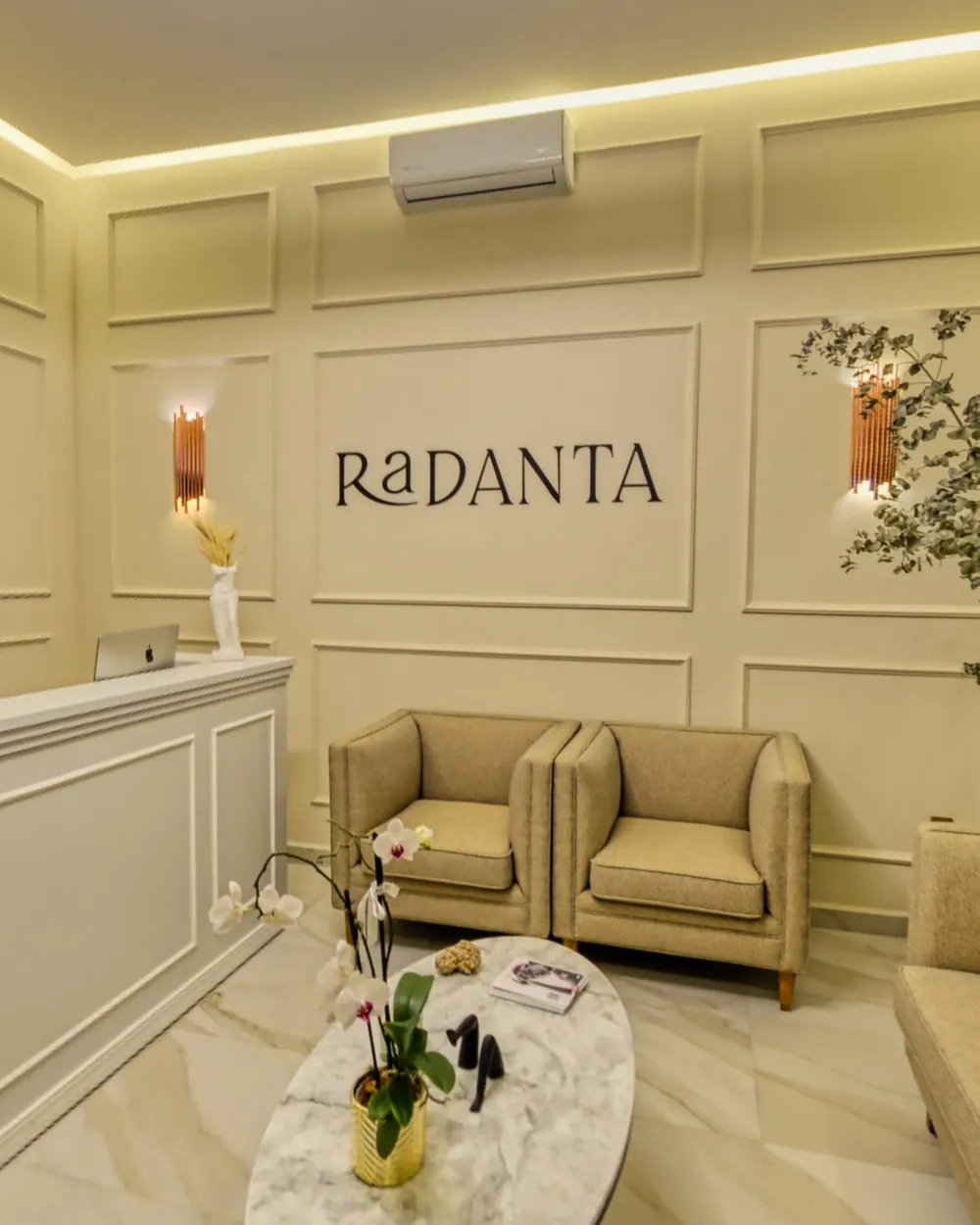 Radanta's reception: a moulded wall with the RaDANTA name, lit sconces, two linen armchairs and an oval marble table.