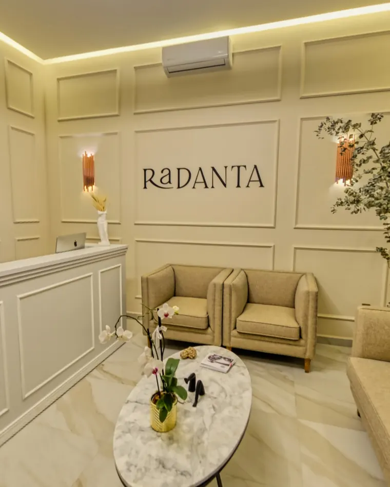 La recepción de Radanta: muro de molduras con el nombre RaDANTA, apliques encendidos, dos sillones de lino y una mesa oval de mármol.