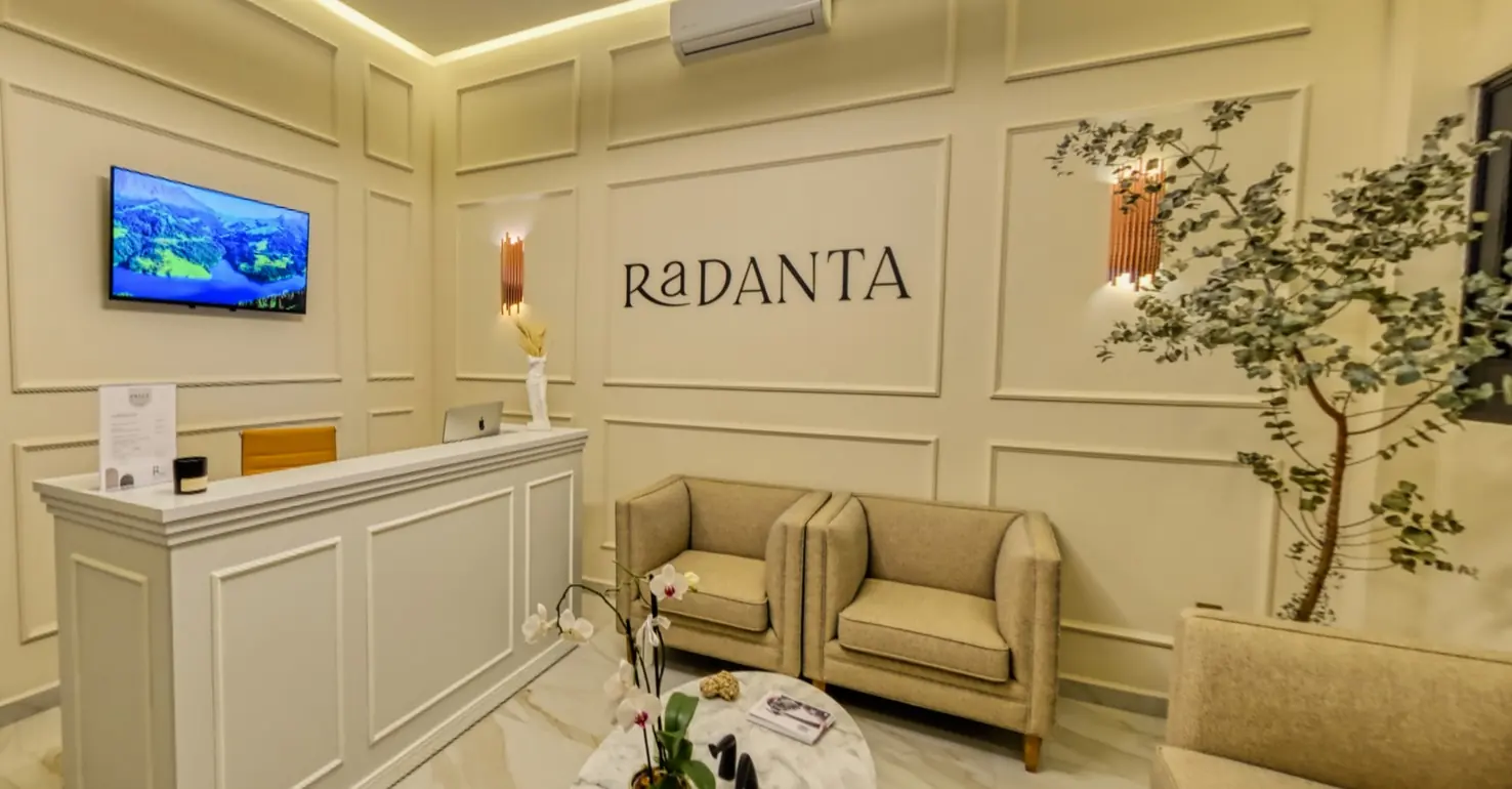 The full reception: a white panelled front desk, the RaDANTA name on the moulded wall, linen armchairs and an olive tree.